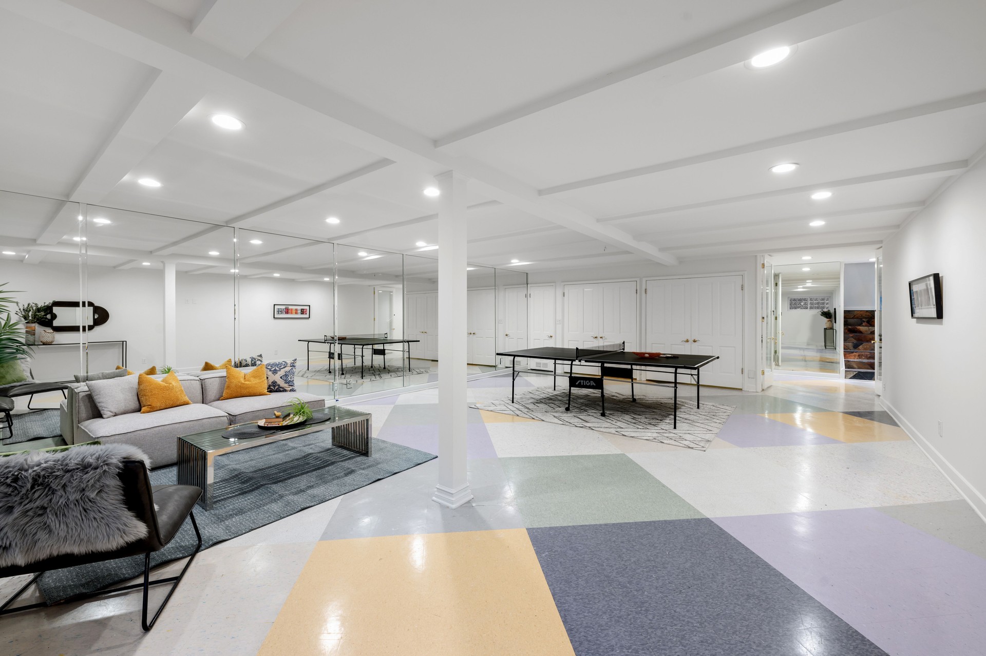 Modern basement interior featuring a ping pong table and cozy seating area with colorful flooring